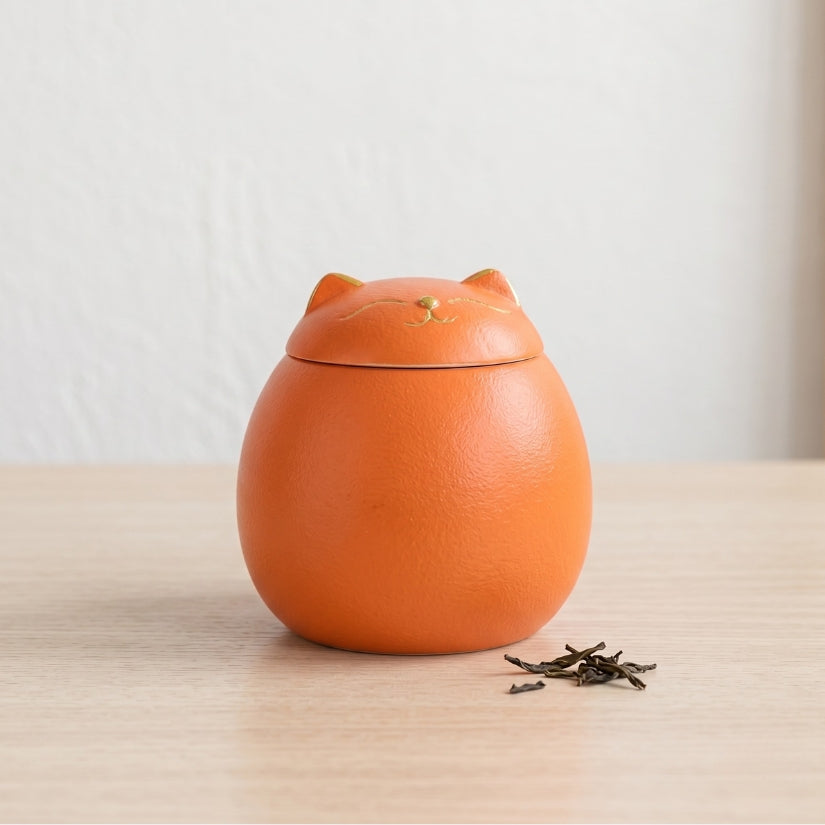 Orange cat-shaped tea canister on a wooden surface with a light background lucky cat, maneki-neko, ceramic tea canister, Japanese kitchen decor, loose leaf tea storage, good luck gift, Asian home decor